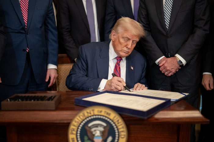 President Donald Trump signs a document while seated at a desk.