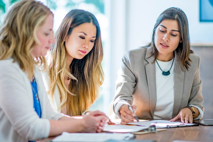 Three people sit around a conference table as one explains figures in a notebook to them.