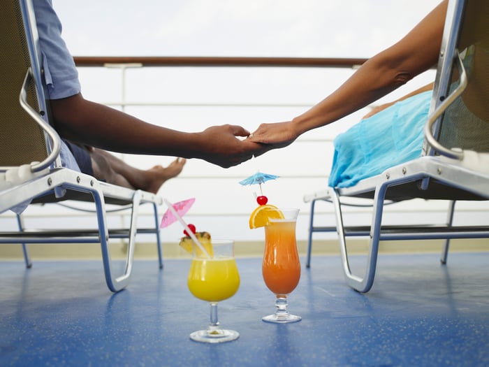Two people holding hands with a pair of tropical drinks between them.
