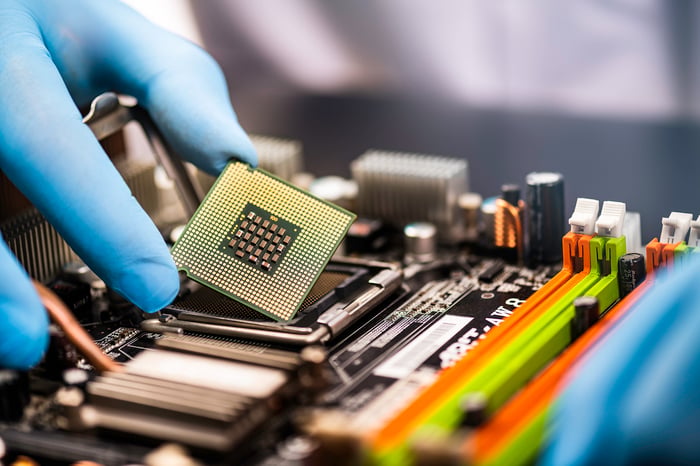 A hand with a latex glove holding a computer chip. 
