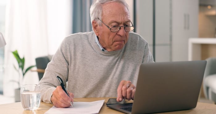 A person taking notes and looking at their laptop.