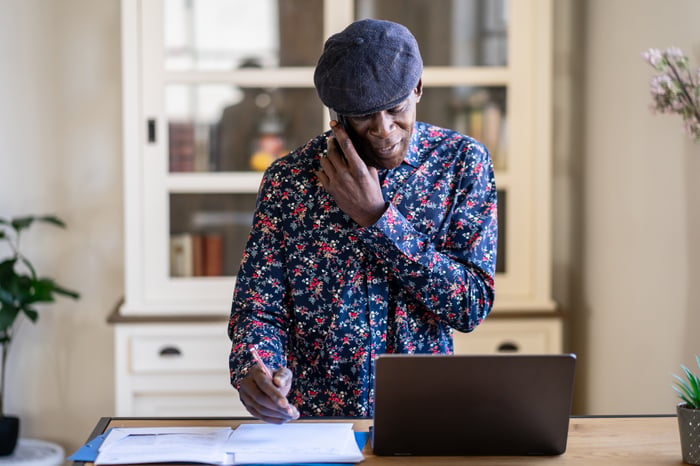 Someone talking on the phone while looking at papers and a laptop.