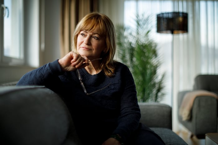 A person sitting on a couch, looking off and thinking.