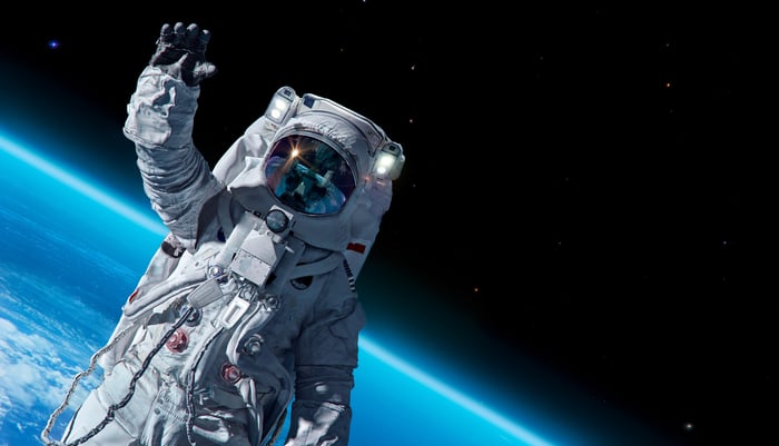 An astronaut waving from outside their ship, with the blue planet and a pure black sky in  the background.  