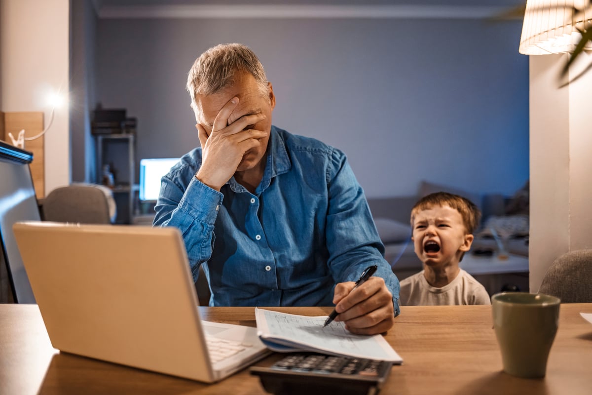 Stressed person writing note in notebook while child cries in background