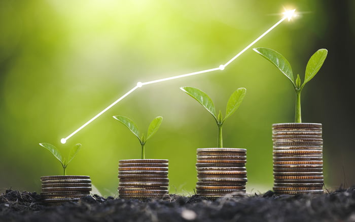 Four stacks of coins in ascending order, with green plants growing out of the top of them.