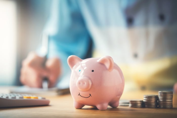 A piggy bank sits on a desk beside coins stacked in ascending columns.