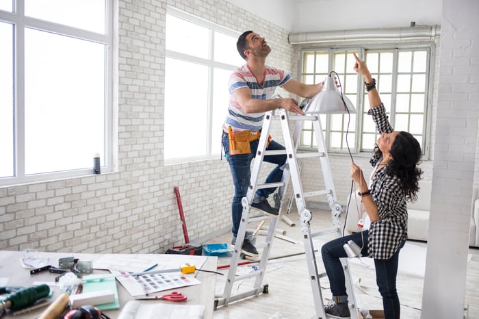 Two people on a ladder working on a home renovation project.