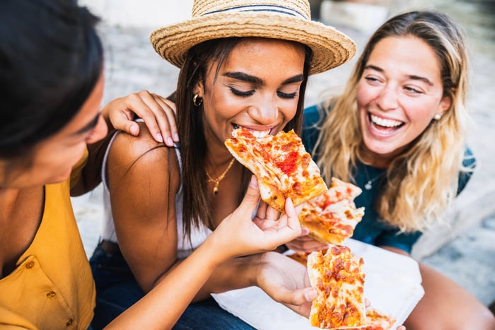 Three women happily eat pizza together.