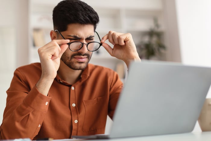 Man squinting with glasses, looking at laptop. 