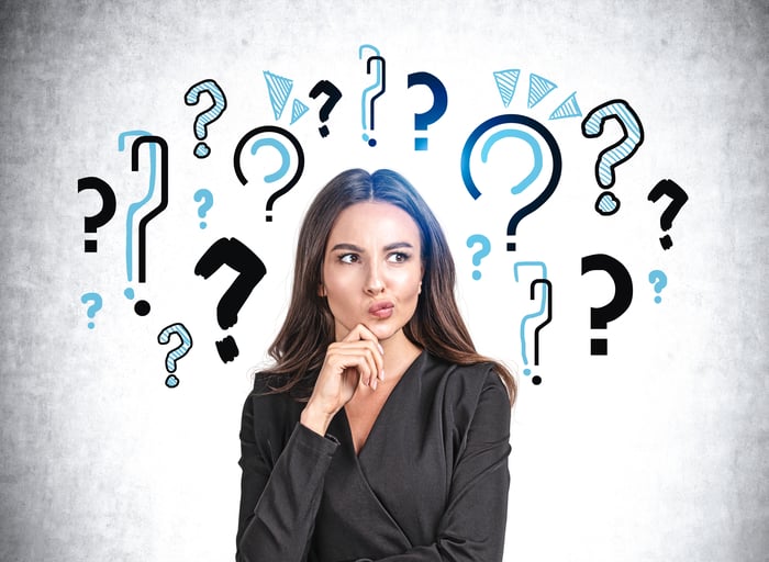 A person holding hand to chin with question marks in the background.