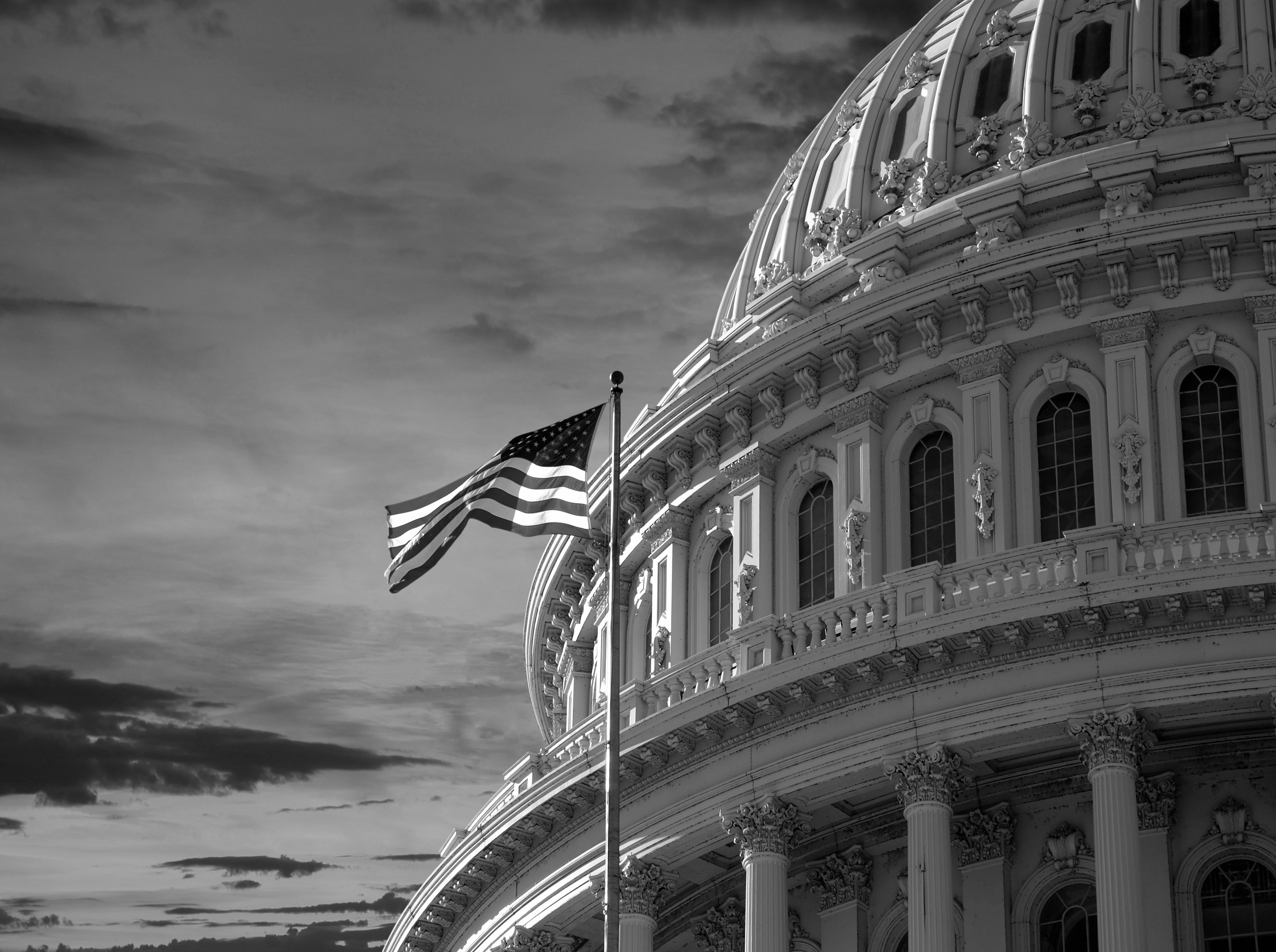 dome of US Capitol Building with American flag waving in foreground -- Washington DC capital politics policy government Congress