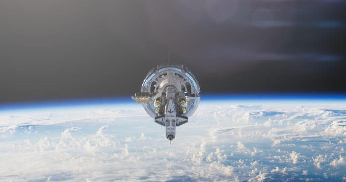A satellite floats in space with clouds and the surface of Earth visible. 
