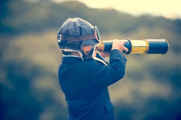 Child in suit looks through telescope.