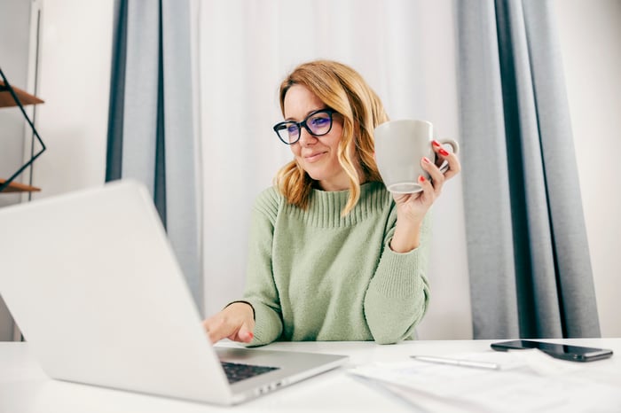 A person at a laptop holding a mug.