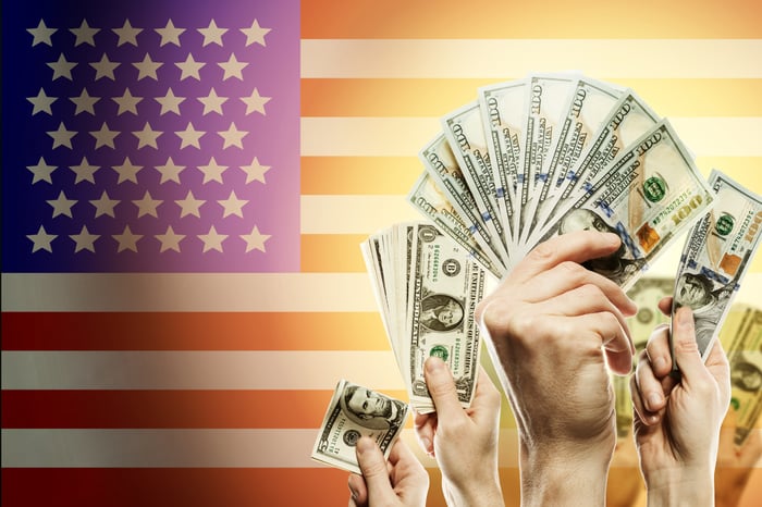 Hands holding money with an American flag in the background.