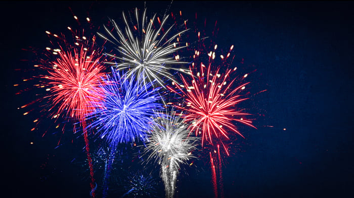 Red, white, and blue fireworks explode in the air at night.