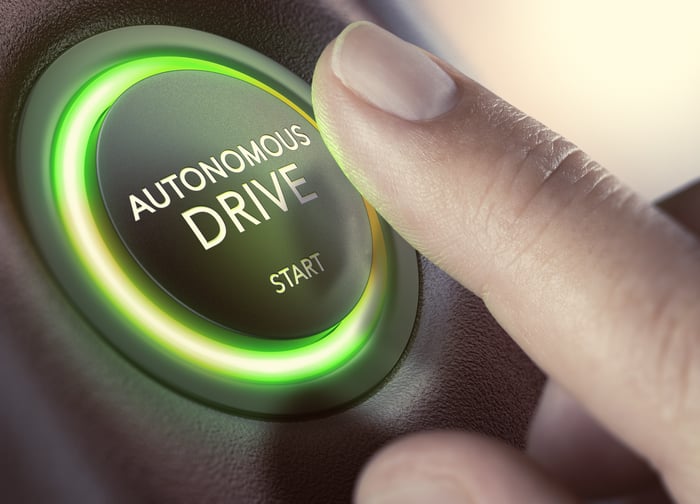 A person tapping an autonomous driving button in a car.