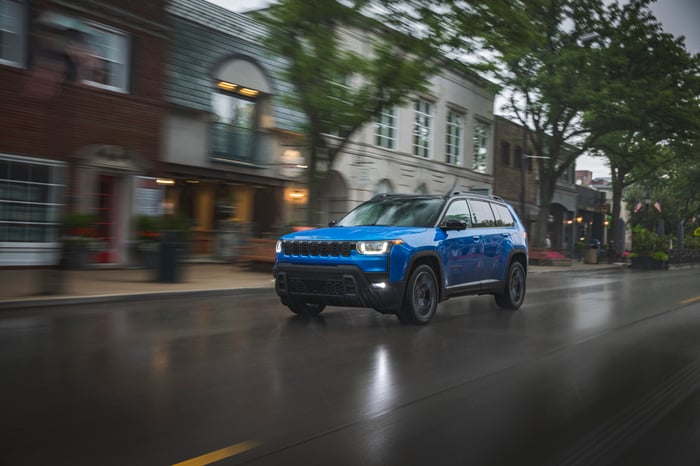 A blue Jeep drives down a city street.