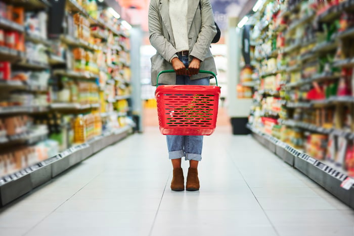 A shopper holds a grocery basket in the middle of a store aisle.