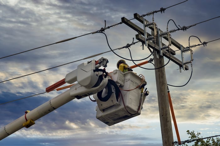 A line-worker sits in a basket attending to wires.