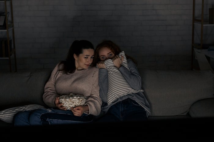 Two people huddling close on a couch as something scary is playing on TV.