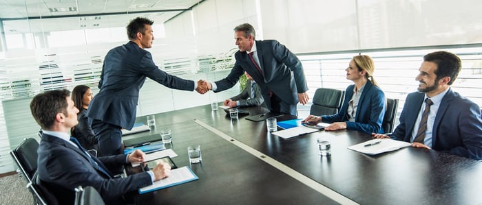 Business people are shaking hands in a boardroom. 