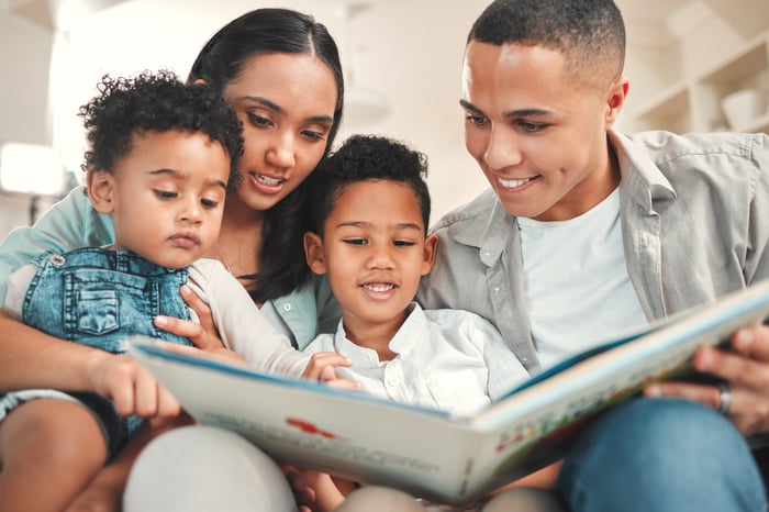 Four people sitting on a couch and looking at an open book.