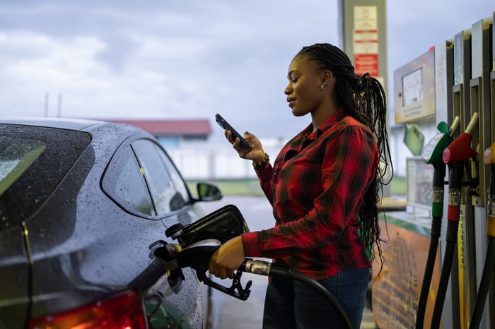 Someone pumping gas while looking at their phone.