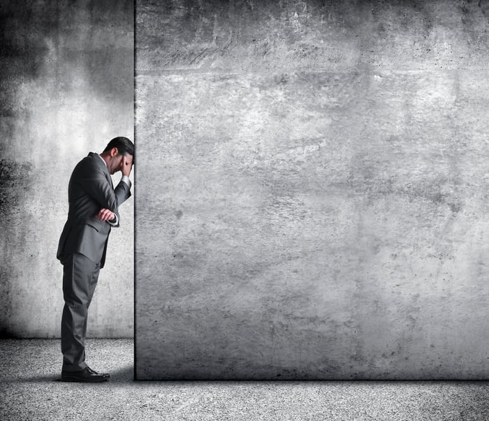 A person in a suit with their head against a wall in worry.