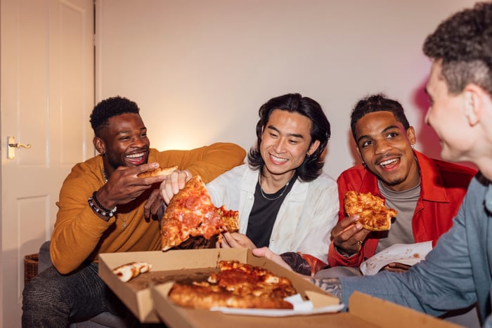 Four smiling people sit around an open box of pizza.