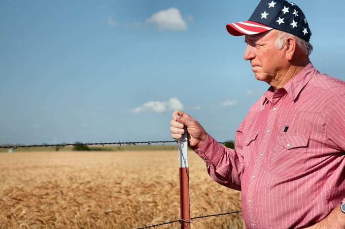 Farmer with an American flag hat on next to a field.