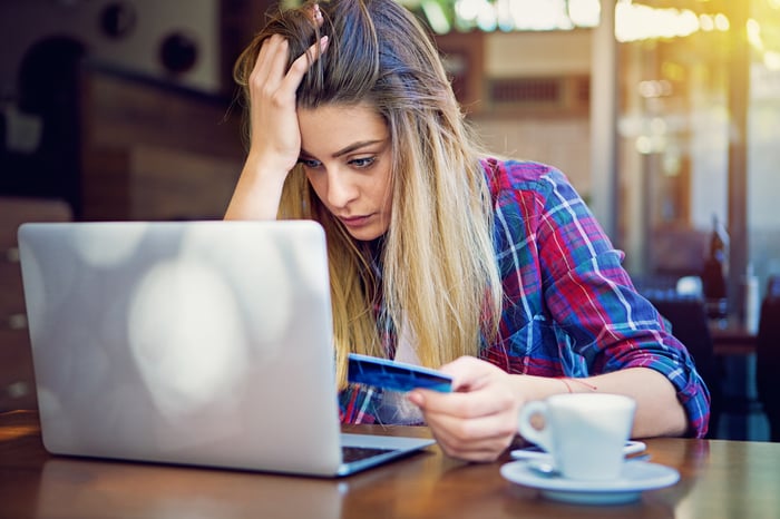 An investor sitting at a cafe in front of a laptop looks frustrated while holding a credit card.