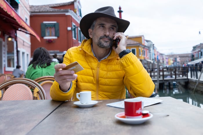 Person sitting outdoors and talking on the phone while holding a credit card.