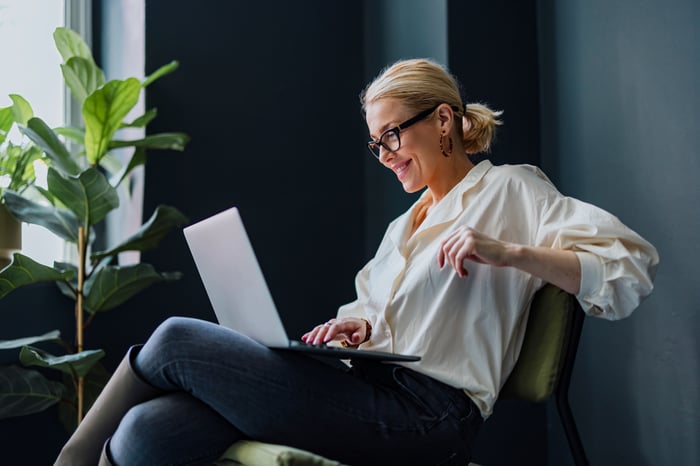 A person sitting in a chair using a laptop and looking pleased at what they're seeing or reading. 