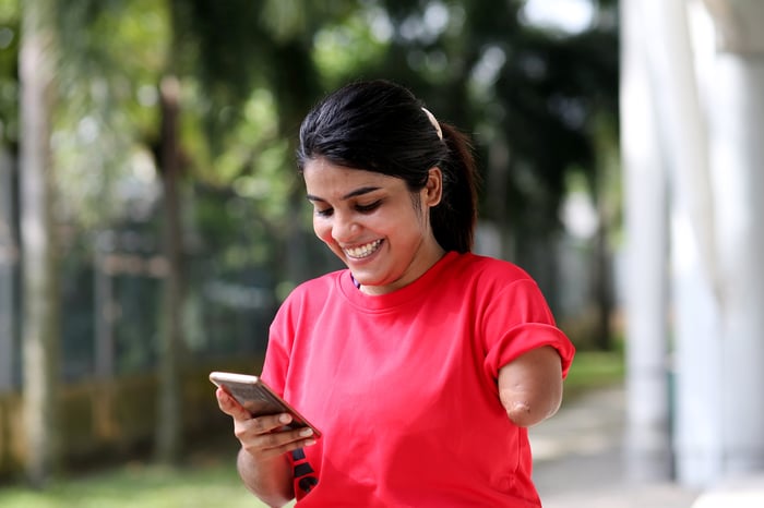 Someone in a red shirt is looking down at her phone and smiling.