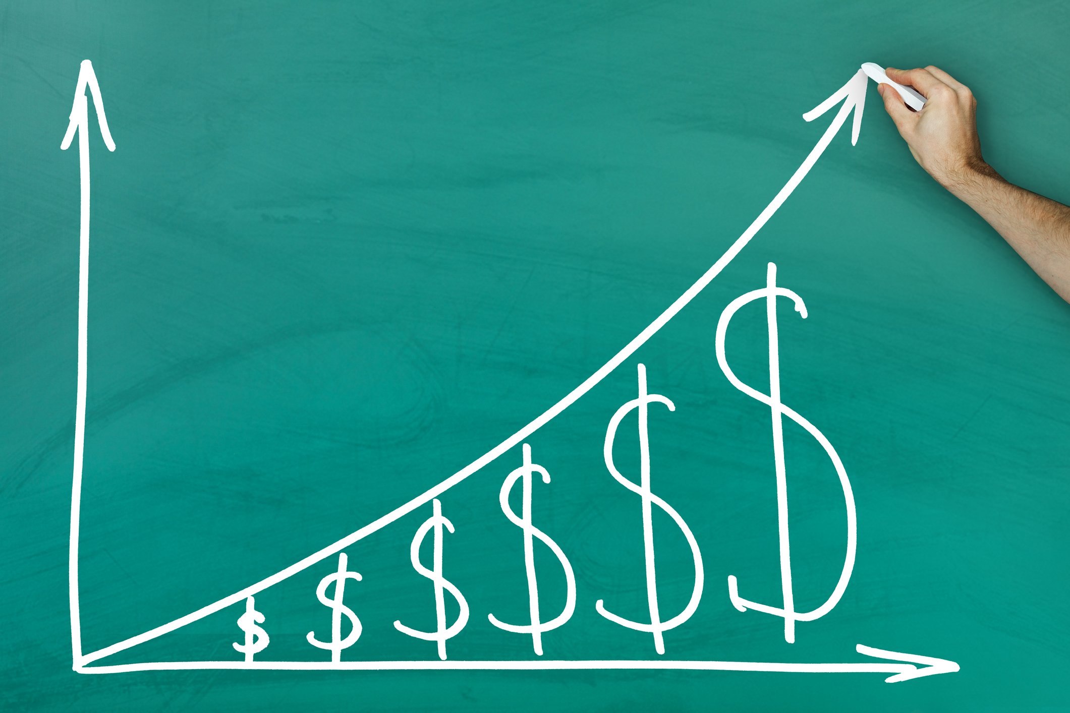A hand drawing money signs and an upward arrow on a chalkboard.