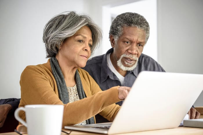 A couple critically reading content on a shared laptop while seated at a table in their home.