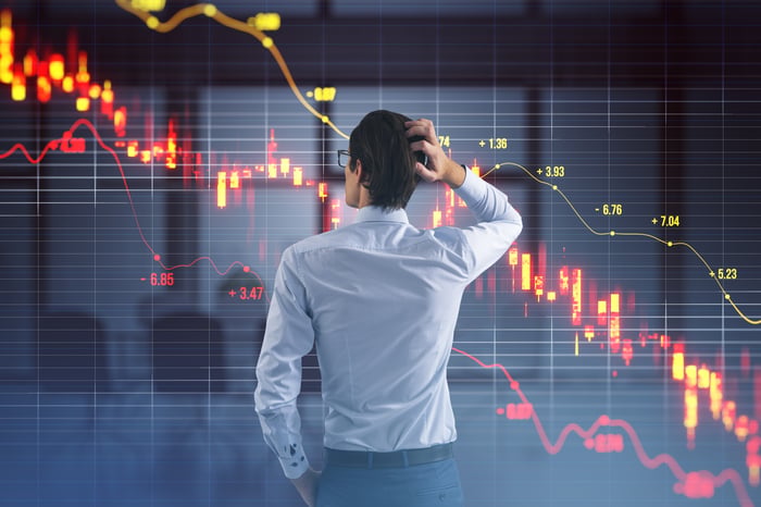 A person scratching head while looking at a steeply declining stock chart.