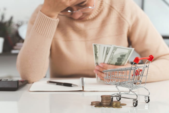 A person looking at a notebook holding money with a shopping cart and some coins nearby.