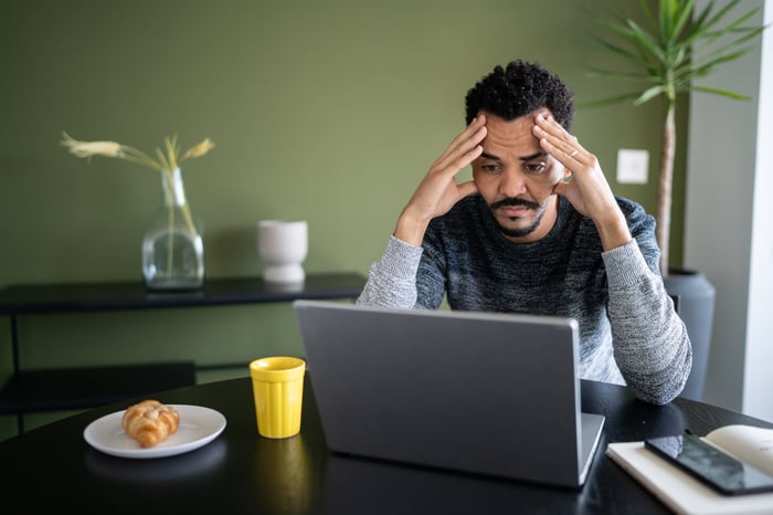 A person at a laptop putting their hands on their head.