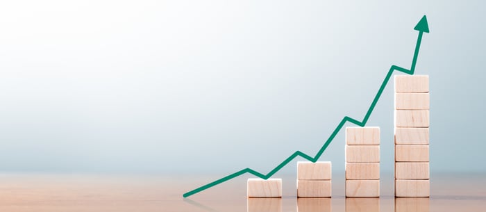 A green chart arrow rises over stacks of wooden blocks.