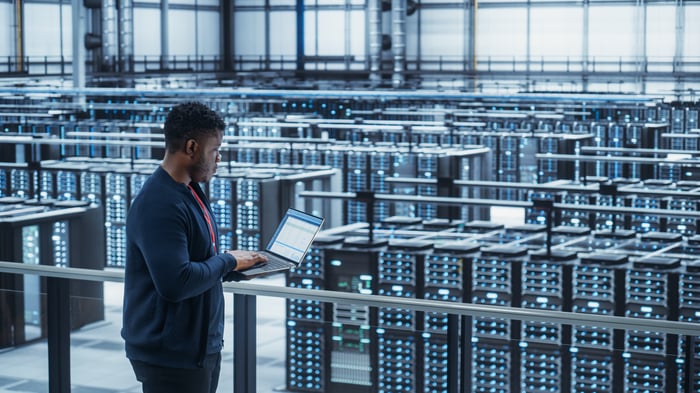 Person looking at an open laptop while standing in a data storage center.