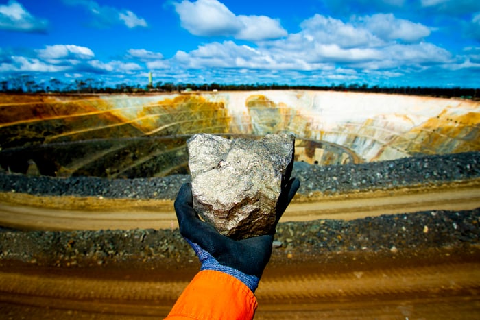 A hand holding silver ore in view of a mining pit.