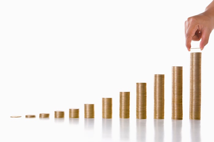 A hand is stacking coins into the shape of a rising bar chart.