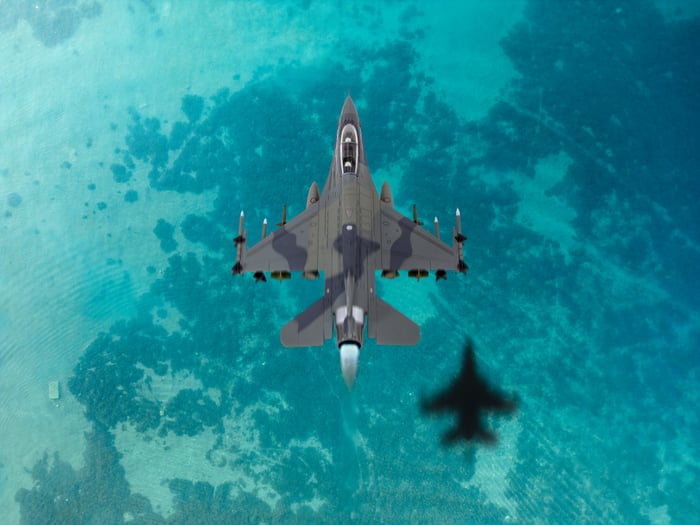 An F-16 Fighter Jet is pictured from overhead flying over the blue ocean. 