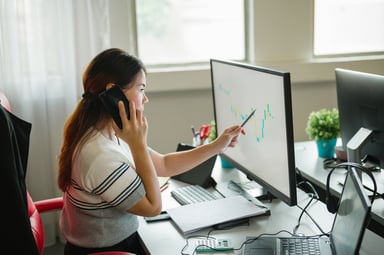 Person on phone while pointing to chart on computer screen