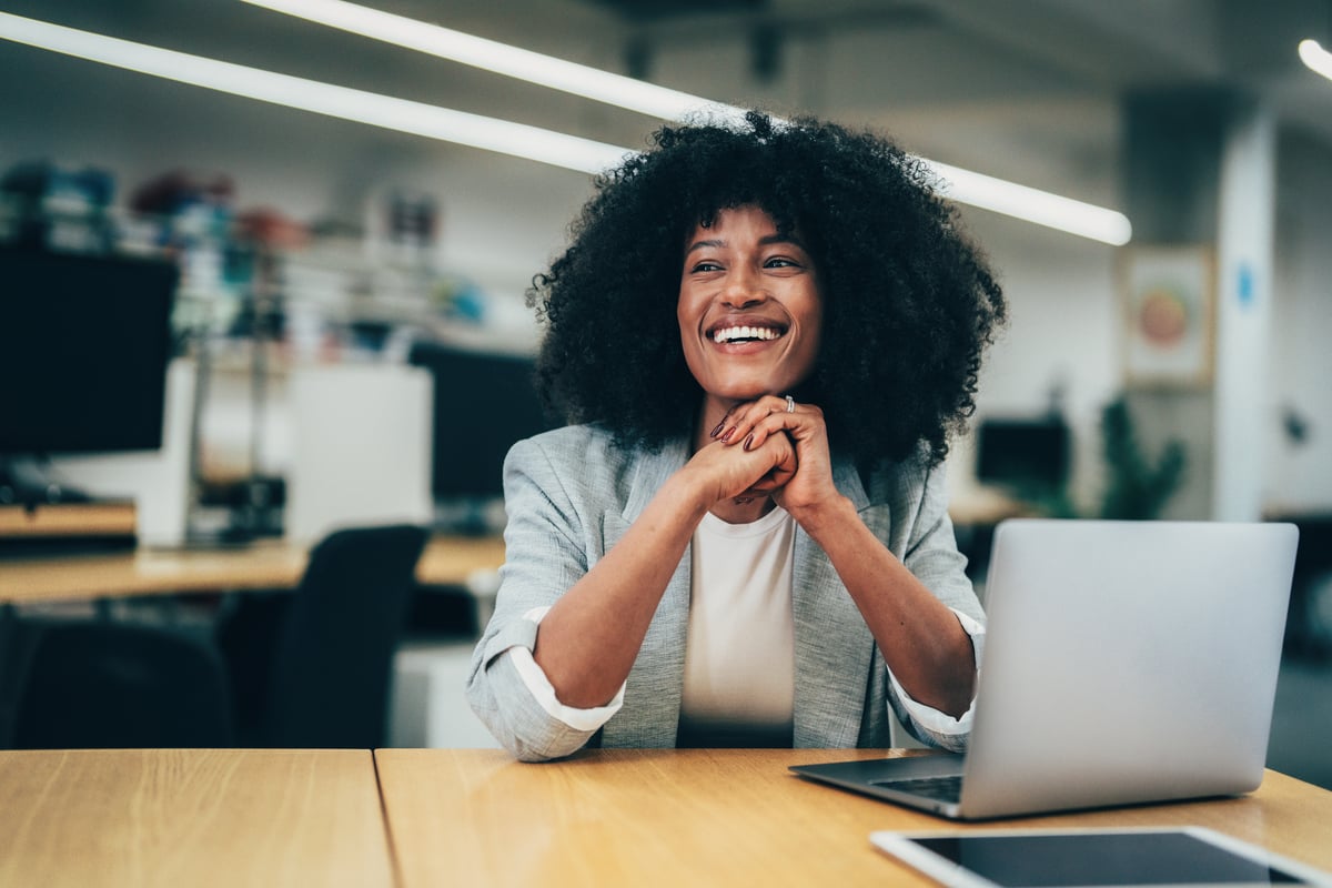 A person smiles while sitting in an office setting in front of a laptop computer.