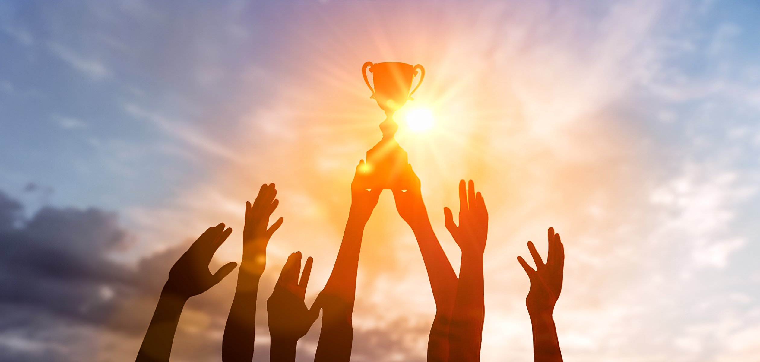 Many hands holding trophy in sunset 1477505250