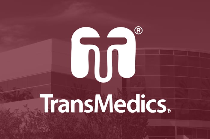 A white TransMedics logo sits on top of a red-hued surgery center.